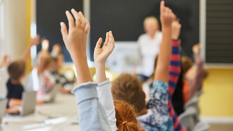 Elever i ett klassrum räcker upp sina händer