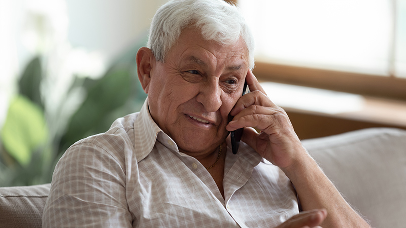 En äldre man ler och talar i telefonen