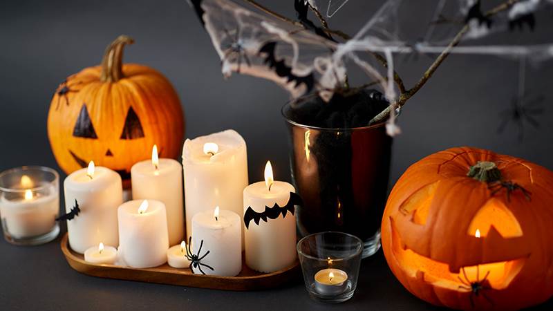 Flera tända ljus dekorerade med fladdermöss av papper och leksaksspindlar, två halloweenpumpor med spindlar på och en vas med dekorationsspindelnät och pappersfladdermöss