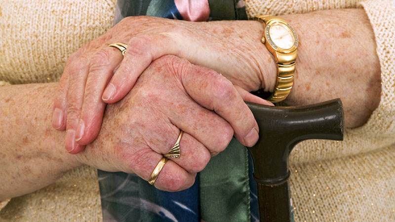 En äldre kvinnas händer som håller i en käpp