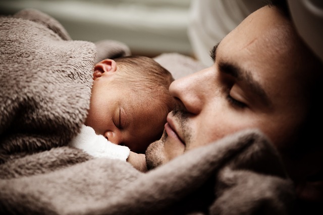 En pappa sover med ett spädbarn på bröstet