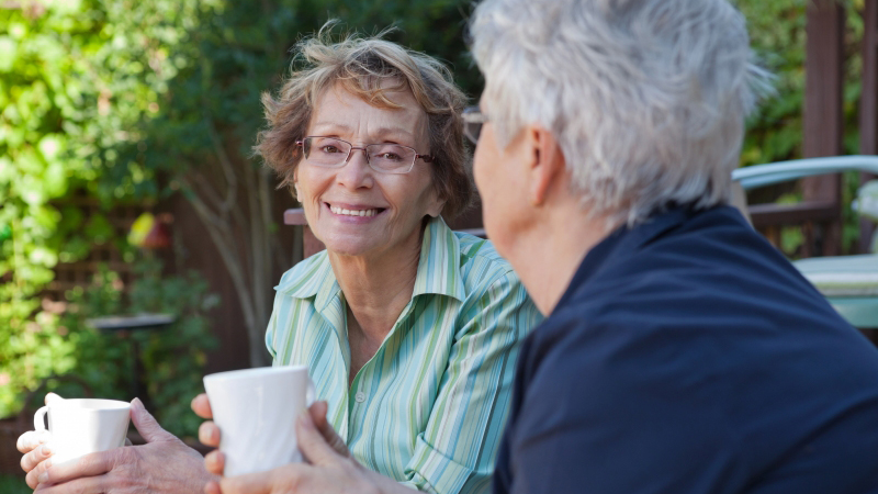 Två äldre kvinnor sitter utomhus och dricker kaffe