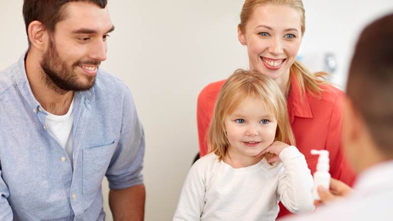 En pappa , en mamma och en liten flicka sitter och samtalar med en läkare