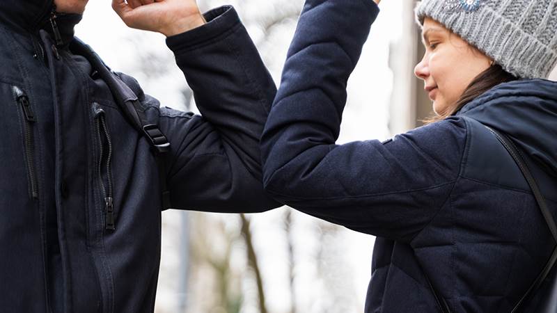 En man och en kvinna i vinterjackor hälsar på varandra på ett coronasäkert sätt med armbågarna