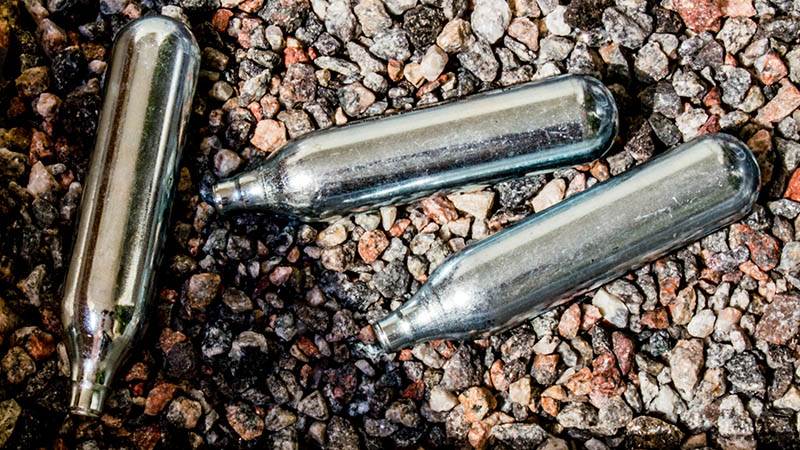 Tre lustgaspatroner ligger på marken.