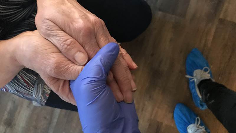 En person med plasthandskar håller i en äldre persons händer