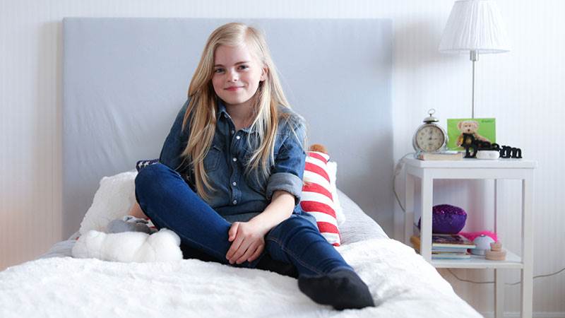 En glad flicka sitter på sängen i sitt rum