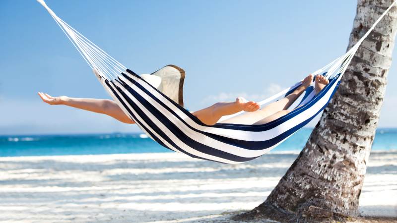 Glöm inte att hänvisa telefonen och att lägga in ett autosvar för din e-post före semestern. En kvinna ligger i en hammock vid en strand.