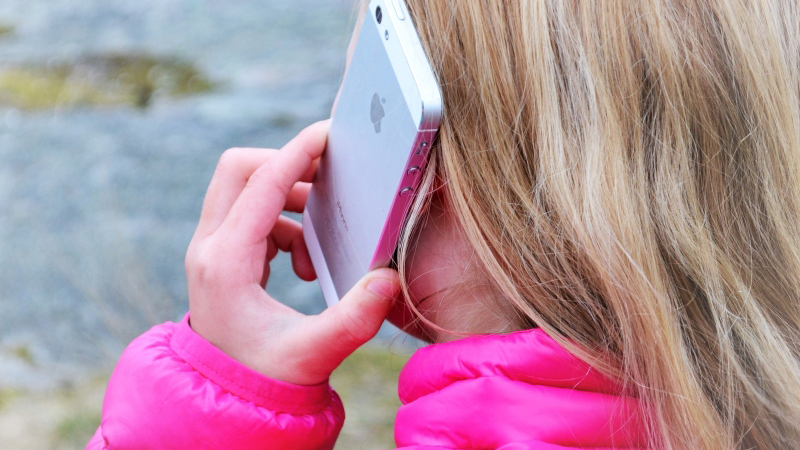 En flicka med långt hår och rosa jacka håller en mobiltelefon mot örat.