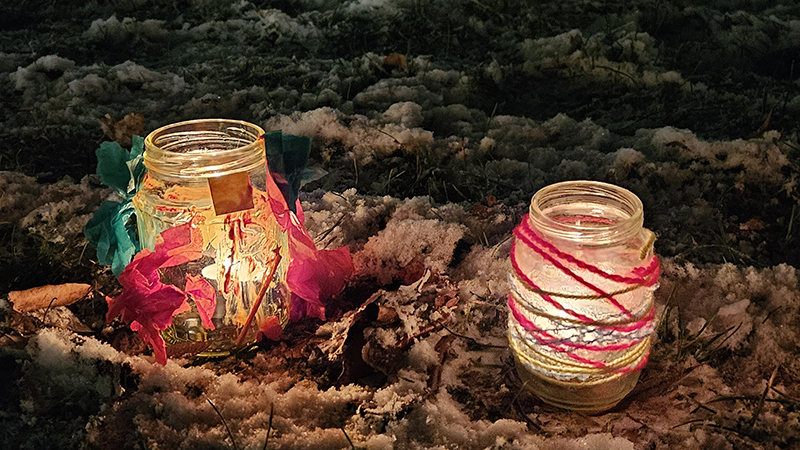 Färgglada ljuslyktor står på mark täckt av snö.