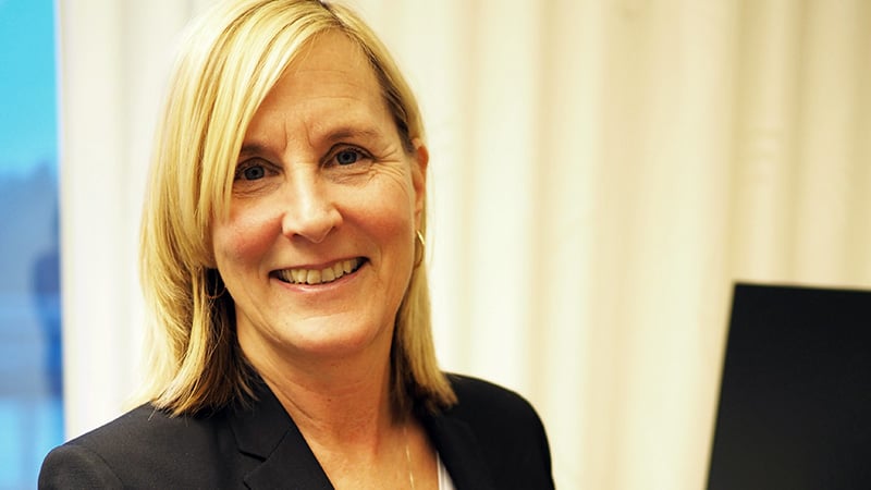 Lotta Wigren En glad kvinna med blont axellångt rakt hår vid skrivbord med datorskäm.