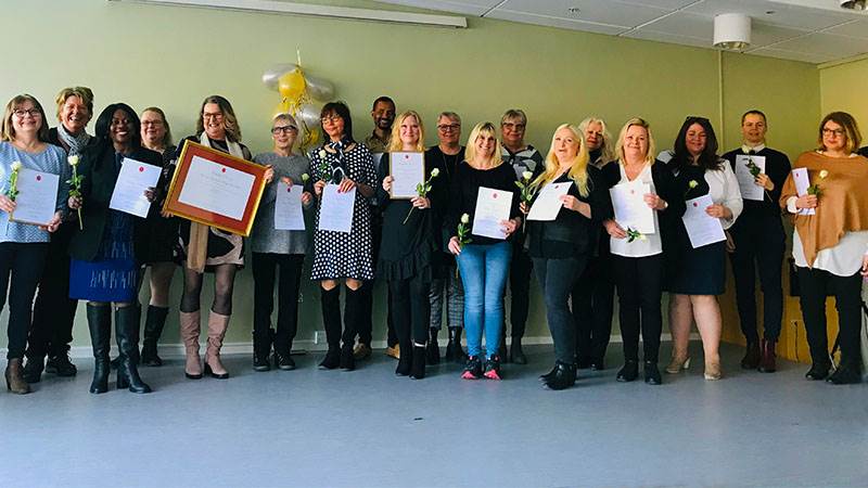 Medarbetarna på dagverksamheterna firar certifieringen på scen tillsammans med en representant från Silviahemmet. En grupp av människor står på en scen och håller upp diplom och blommor