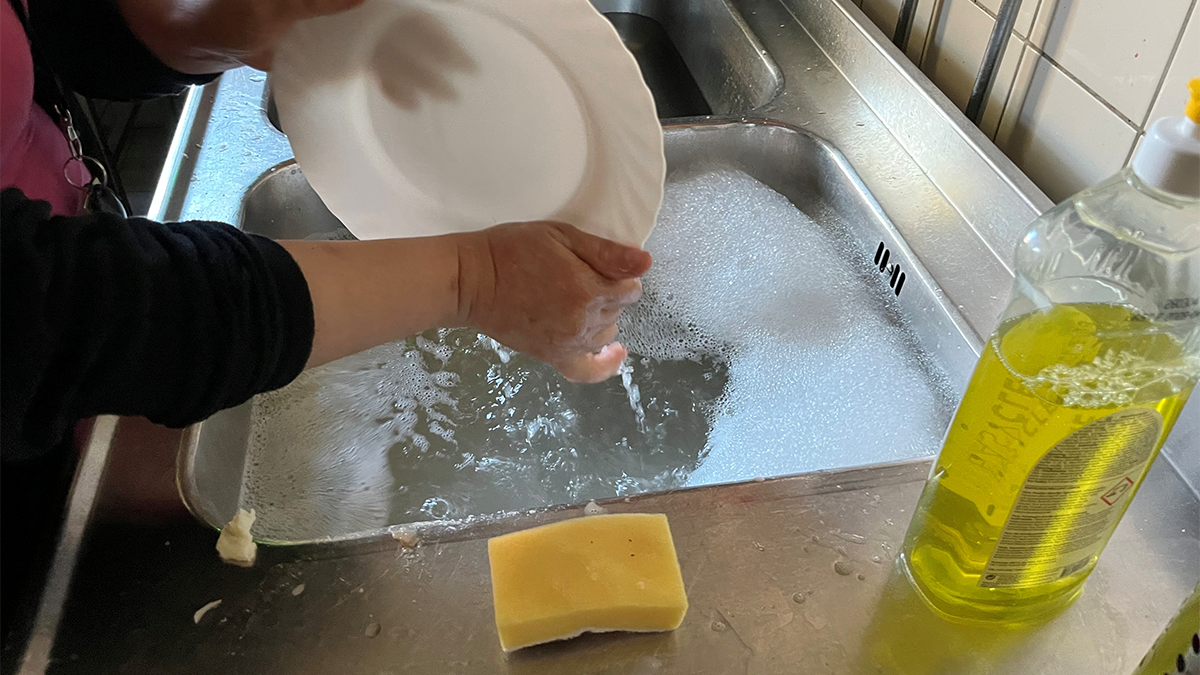 Två händer i diskhon med ett vitt fat.