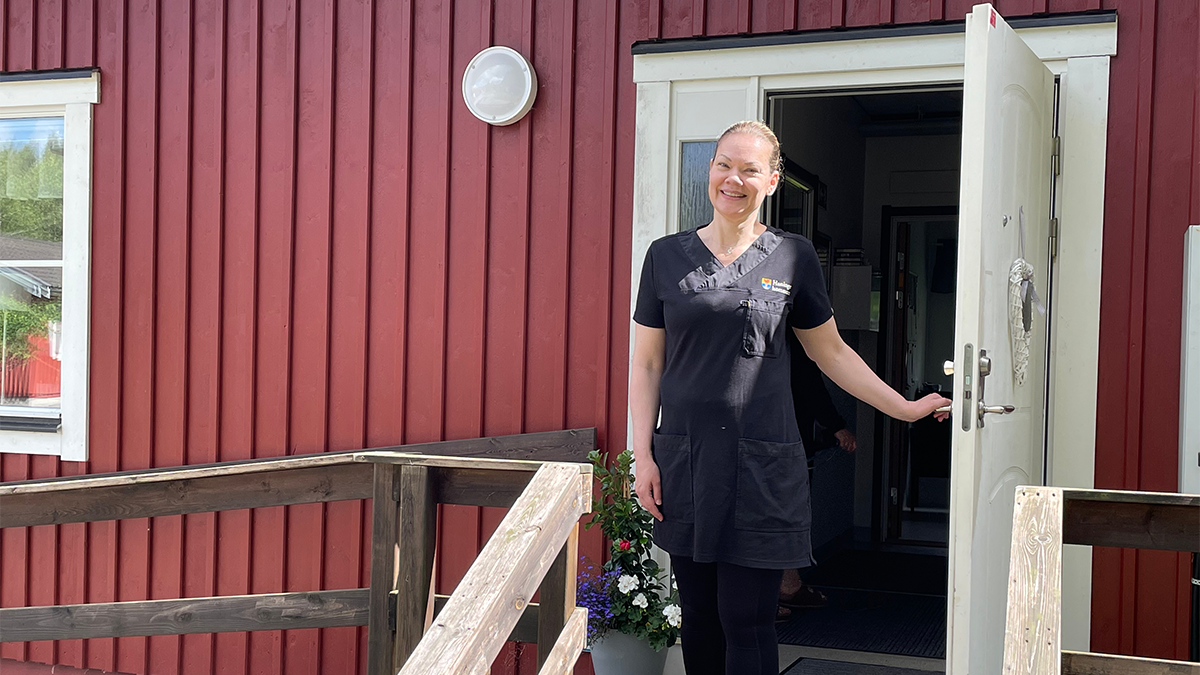 En kvinna öppnar dörren till ett rött hus.