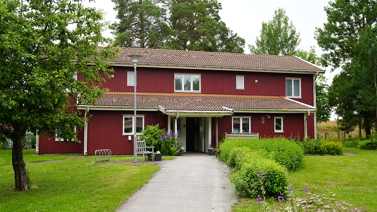 Ett rött tvåvåningshus i en trädgård på sommaren. 