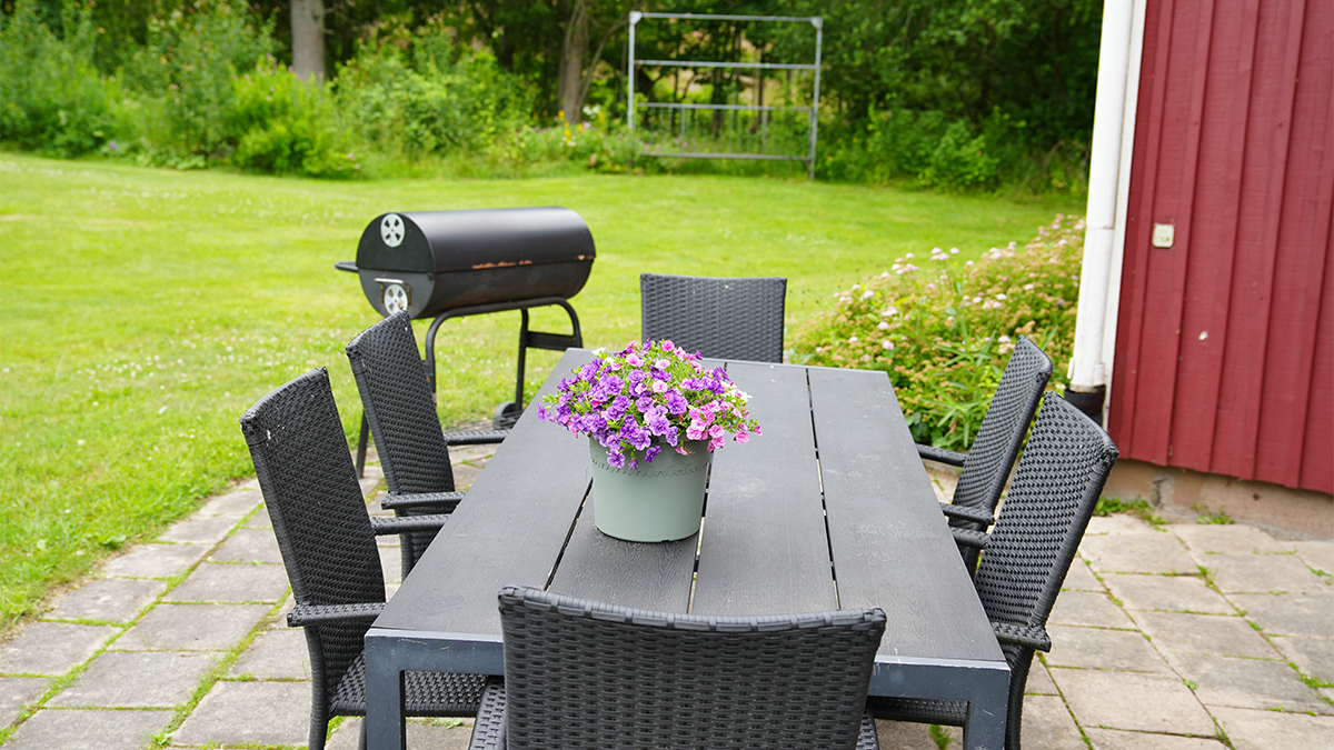 En uteplats i gröngräset med grill bakom. 
