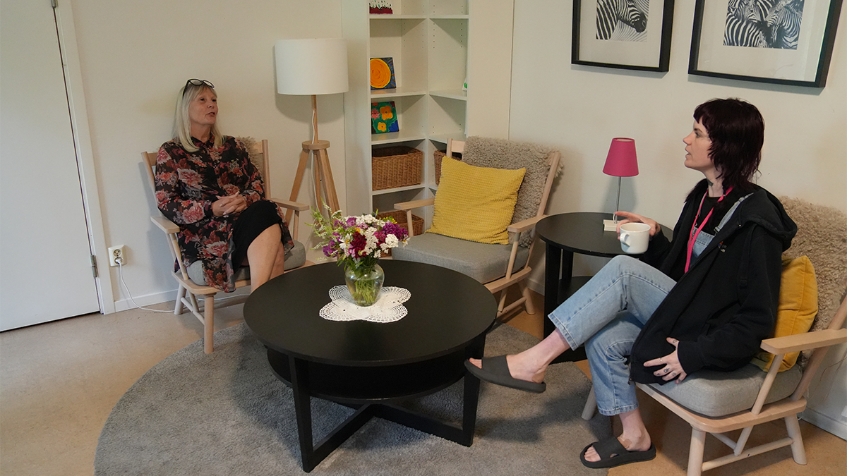 Två personer samtalar i två fåtöljer. 