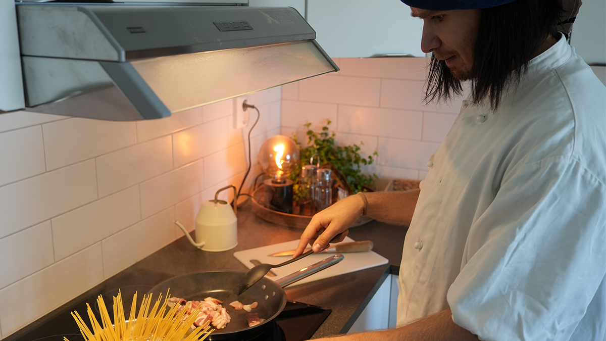 En person lagar spaghetti och bacon på spisen. 