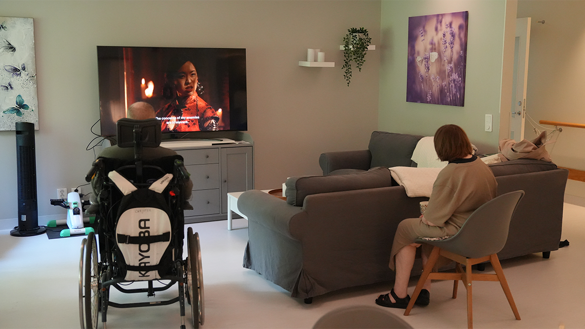 Två personer ser på film, en sitter i rullstol. 