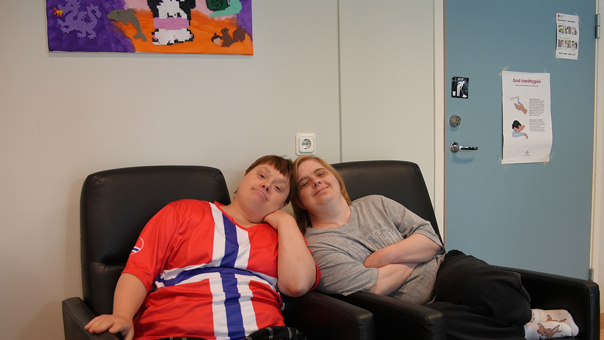 Två personer lutar huvudet mot varandra sittande i varsin stol.