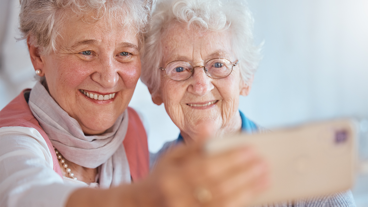 Två äldre damer tar en selfie med mobilen. 