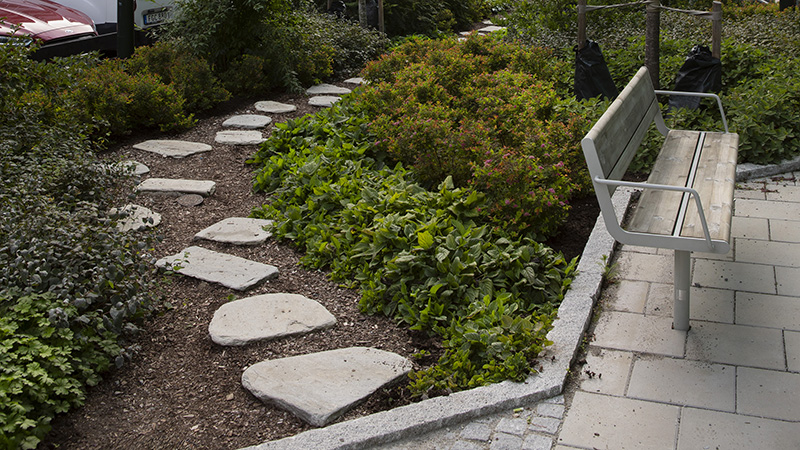 Sittplats i form av soffa omgiven av växtlighet och gångplattor i sten