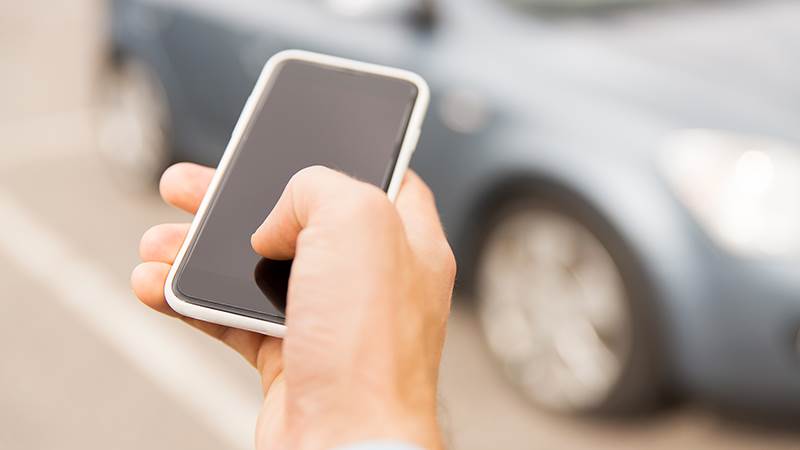 närbild på en hand som håller en mobiltelefon framför en bil