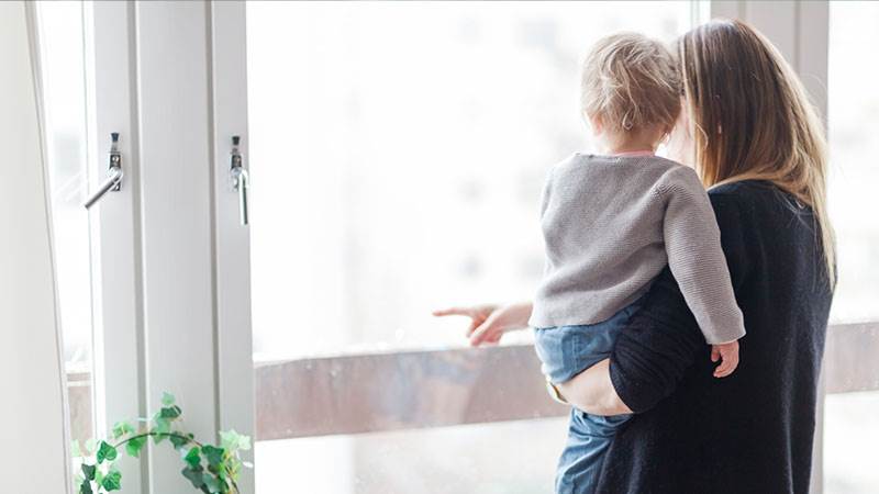 En mamma håller ett barn i famnen och pekar ut genom fönstret