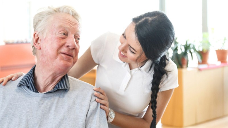 En äldre man sitter och pratar med en sköterska inomhus