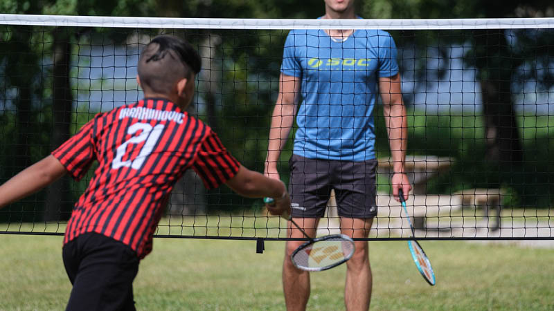 En pojke spelar badminton med en man på en sommardag.