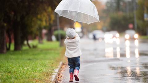 Liten flicka går i regnet med ett uppfällt paraply ovanför sig. 