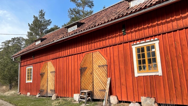 Röd lada med träfasad, orangea fönster och två dörrar i trä. 