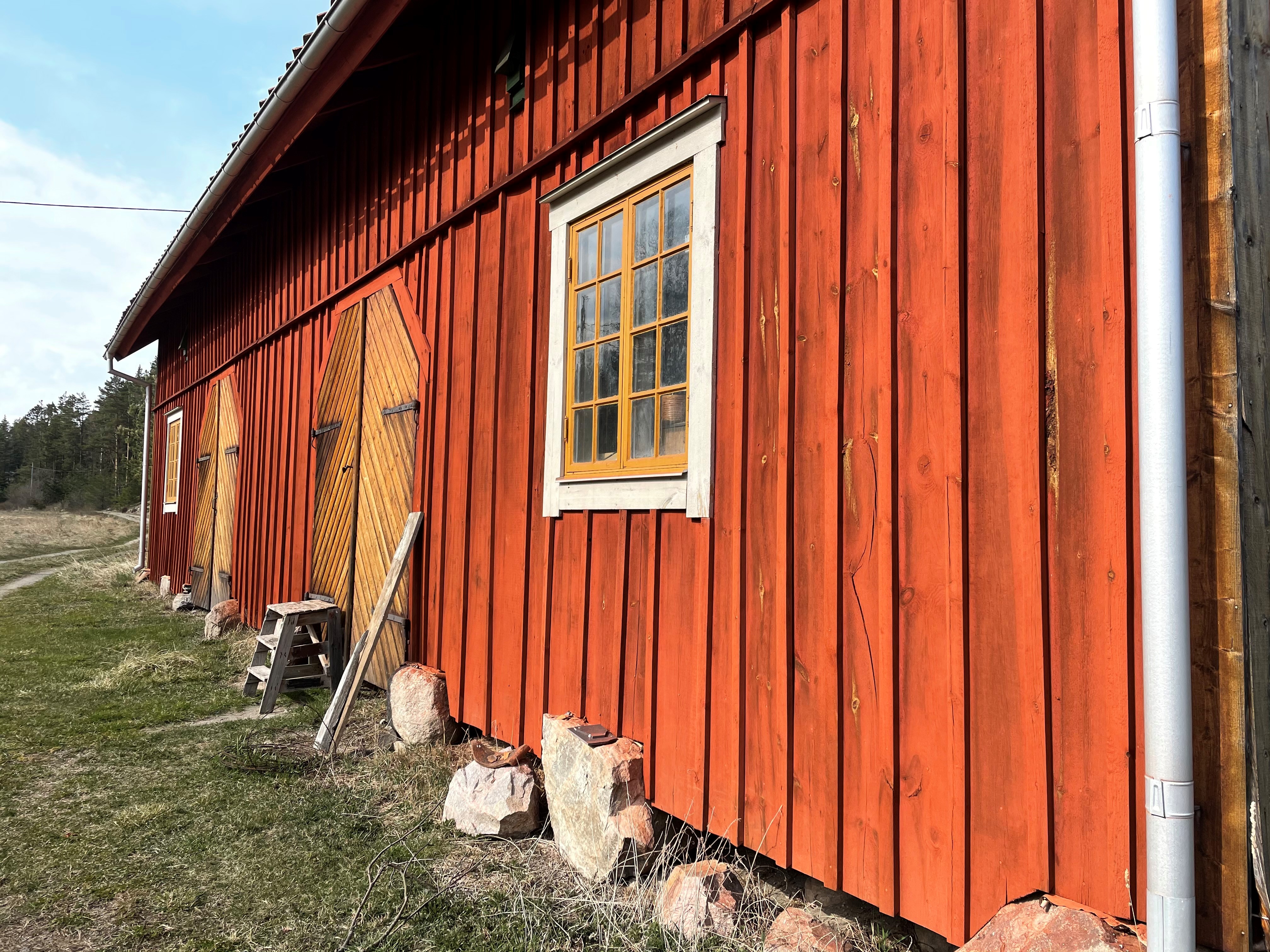 En röd träfasad målad med röd slamfärg. På fasaden finns två fönster och två dörrar målade i gul ockra.