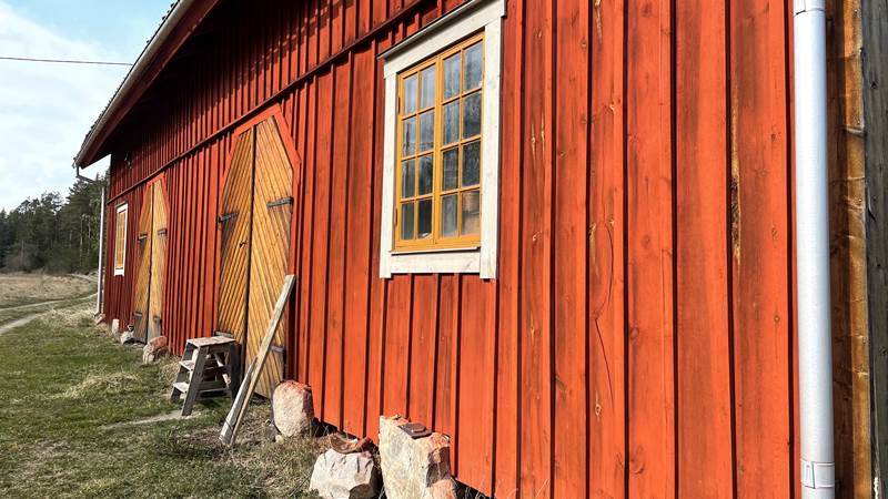 En röd träfasad målad med röd slamfärg. På fasaden finns två fönster och två dörrar målade i gul ockra.