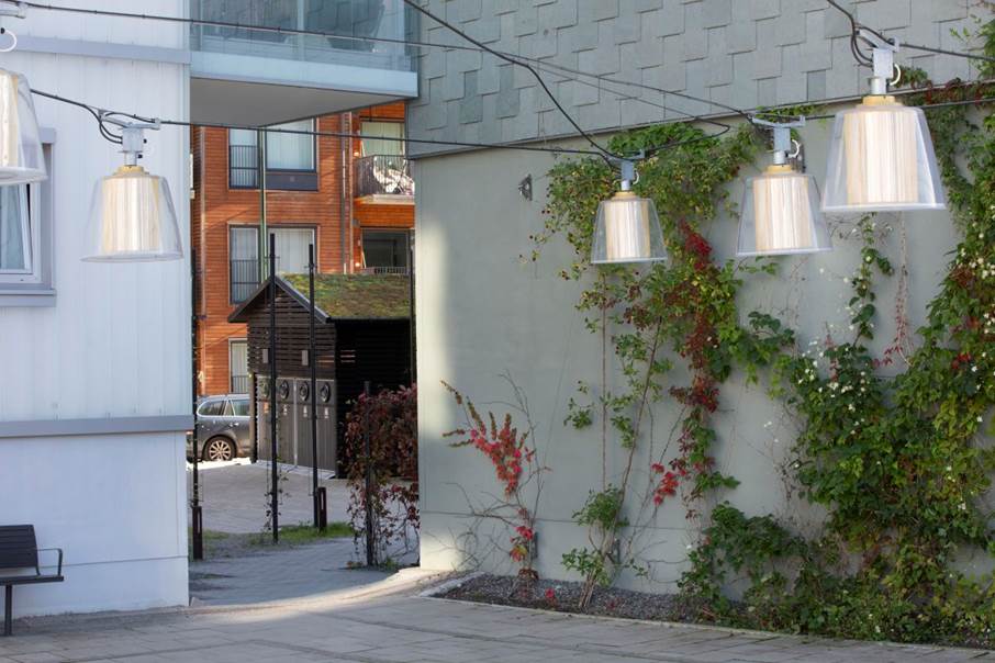 En omhändertagen och välkomnande plats som relaterar till den mänskliga skalan, Vega. Innergård fotad ut mot gatan, till höger i bild en husfasadsvägg i grått prydd med växtlighet.