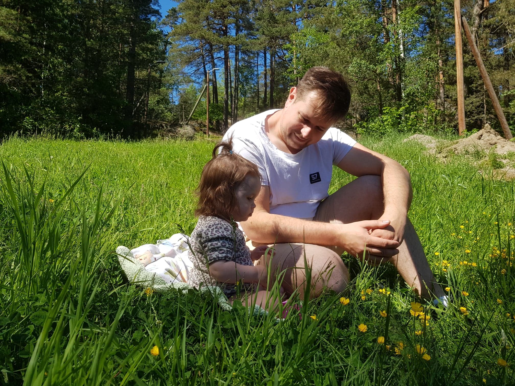 En pappa sitter med sin lilla dotter i gräset