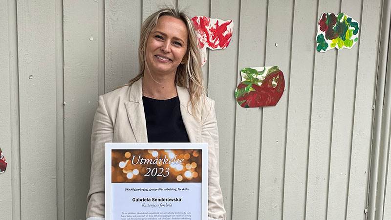 Gabriela Senderowska, förskolelärare vid Kastanjens förskola. Kvinna i halvfigur håller utmärkelse utomhus framför skolbyggnad.