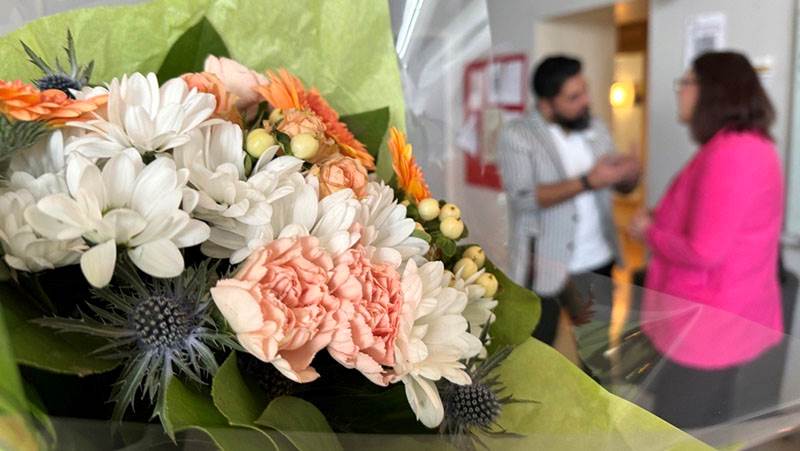 Blombukett i papper i fokus. En man och en kvinna står i bakgrunden och kommunicerar.