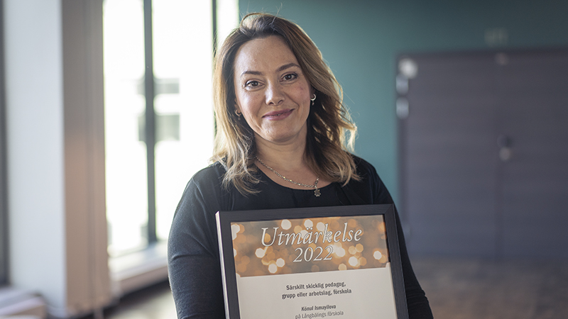 En leende kvinna i mörkt långt hår håller ett diplom