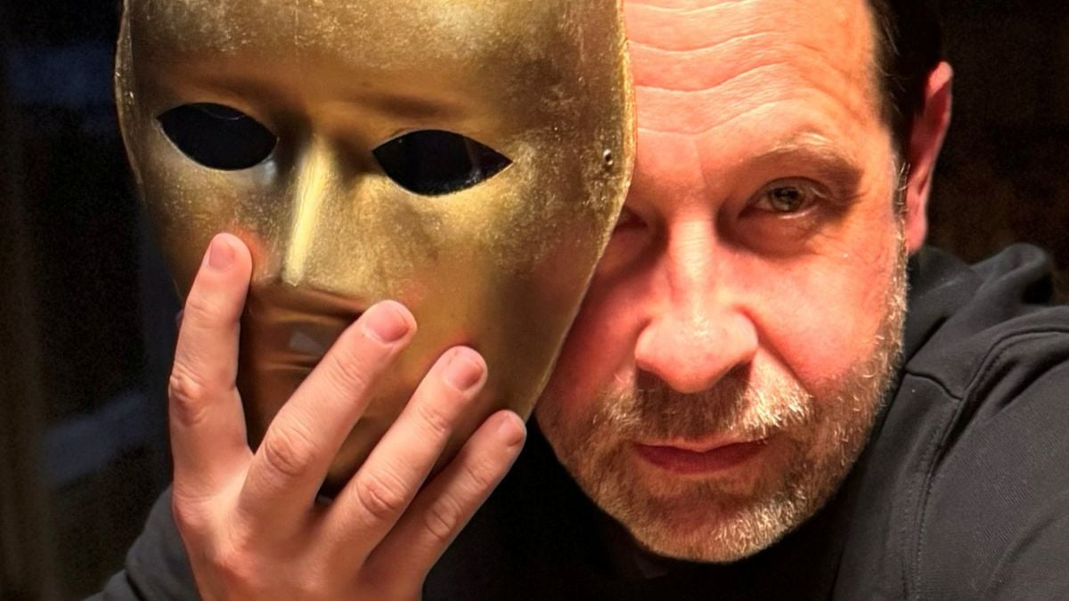 Närbild på ansikte med händer som håller en gyllene mask på sidan om ansiktet
