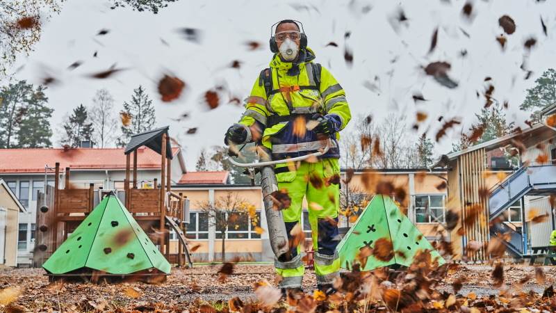 Feriearbetare blåser löv med lövblås på Hagaskolans skolgård