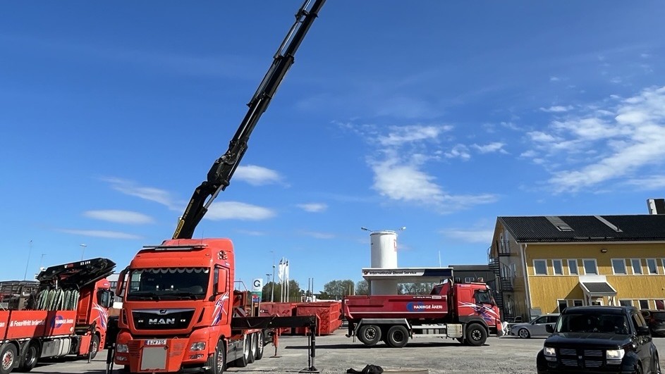 Röd kranbil fotat utomhus med kranen fullt utvecklad högt upp i luften. Fotat från distans.