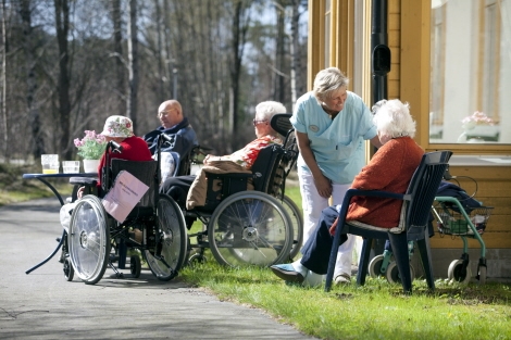 Äldre personer sitter i rullstolar eller vanliga stolar utomhus på Malmgårdens äldreboende
