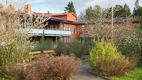 Vallagården - en orangeröd tegelbyggnad med vit balkong och mycket växter utomhus.