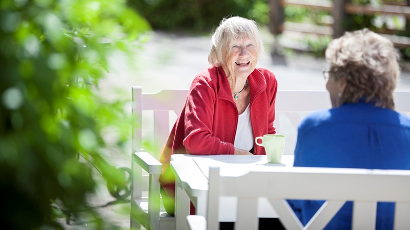 Två kvinnor skrattar vid ett fikabord utomhus