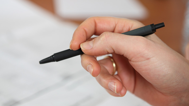 Närbild på en hand som håller en penna över ett papper