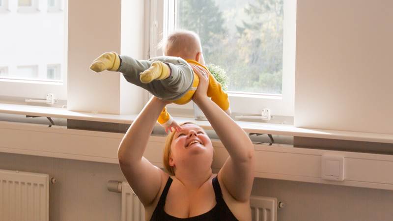 Mamma lyfter barn över huvudet och ler.
