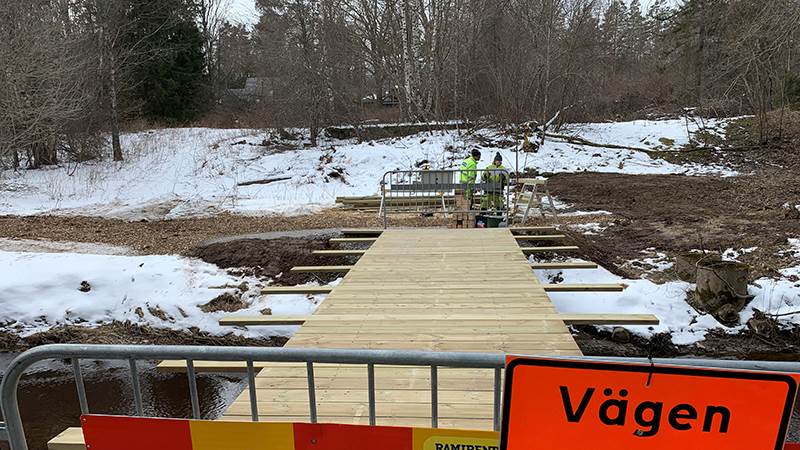 Byggnation av gångbro i trä över en å.