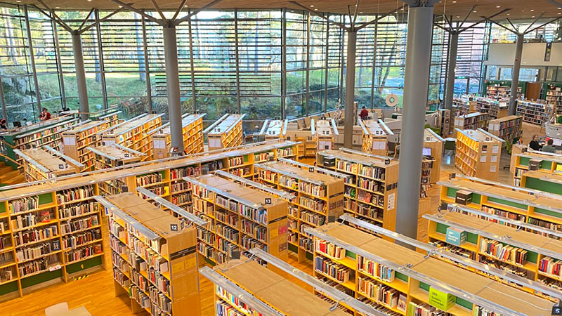 Biblioteket i Handen. Flera bokhyllor står uppställda framför stora glasväggar ut mot en park.