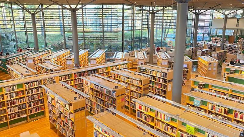 Biblioteket i Handen. Flera bokhyllor står uppställda framför stora glasväggar ut mot en park.